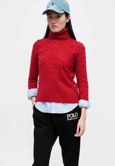 Pulover roșu din tricot, cu guler înalt, purtat peste o cămașă bleu deschis, asortat cu pantaloni de trening negri, cu logo-ul alb "Polo Ralph Lauren".