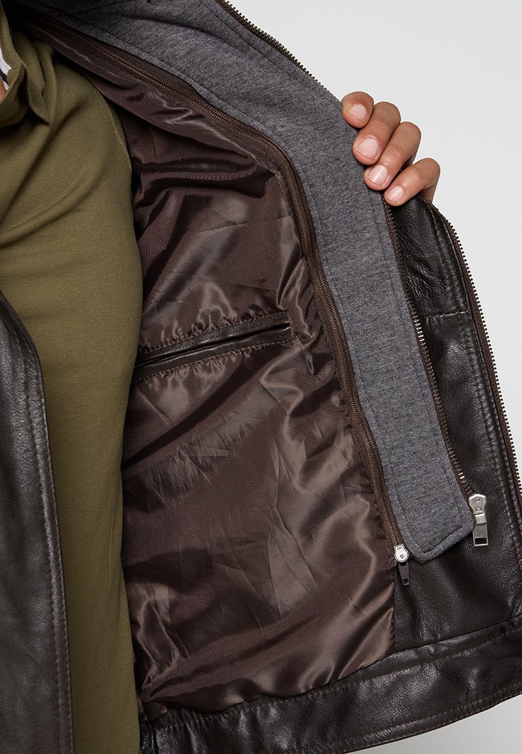 Chaqueta de cuero marrón con un forro gris. El interior presenta un acabado marrón suave y un bolsillo con cremallera. Se muestra el cierre de cremallera en el lateral.