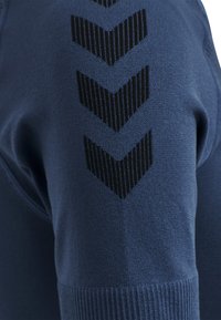 Sweat-shirt en polaire bleu marine avec un motif chevron noir texturé le long de l'épaule, doté de poignets côtelés et d'une finition lisse.