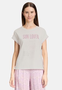 Vaaleanharmaa puuvillateeppari, jossa on rullatut lyhyet hihat, ja jossa on "SUN LOVER" -teksti vaaleanpunaisilla niiteillä sekä hillitty teksti alla. Yhdistetty kuvioituihin violetteihin housuihin.