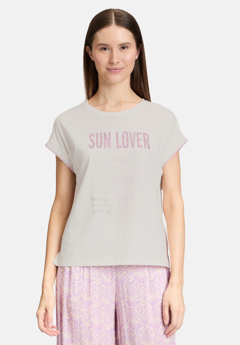 Vaaleanharmaa puuvillateeppari, jossa on rullatut lyhyet hihat, ja jossa on "SUN LOVER" -teksti vaaleanpunaisilla niiteillä sekä hillitty teksti alla. Yhdistetty kuvioituihin violetteihin housuihin.