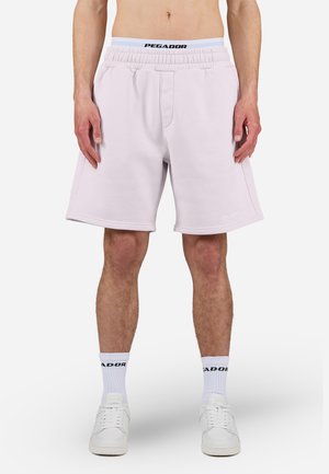 Shorts en sweat rose clair avec une taille élastique arborant le logo "PEGADOR". Texture lisse, longueur genou et coutures latérales discrètes.