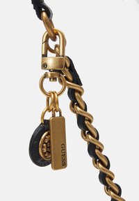 Mosazný řetězový popruh propletený s černou kůží, s mosaznou sponou a dvěma visícími štítky, z nichž jeden je gravírovaný s logem "GUESS".