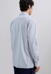 Camisa de manga larga a rayas en azul y blanco con cuello clásico y puños abotonados. Cuenta con un bajo recto y un yugo trasero para mayor estructura.