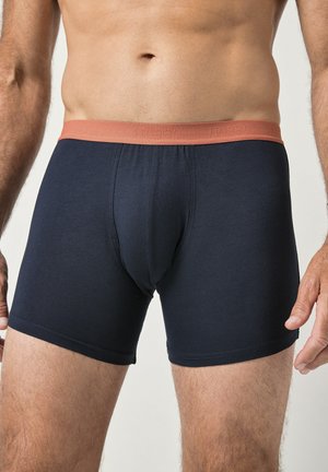 Navyblaue Boxershorts mit einem kontrastierenden korallenfarbenen Bund, gefertigt aus einem glatten, elastischen Stoff mit enger Passform und ohne Muster.
