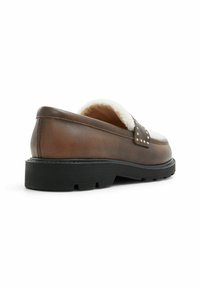 Ruskean nahka-loaferit, joissa on teksturoitu pinta, lammasvillavuori, niitteillä koristeltu hihna ja musta kumipohja, joka sisältää uria pidon parantamiseksi.
