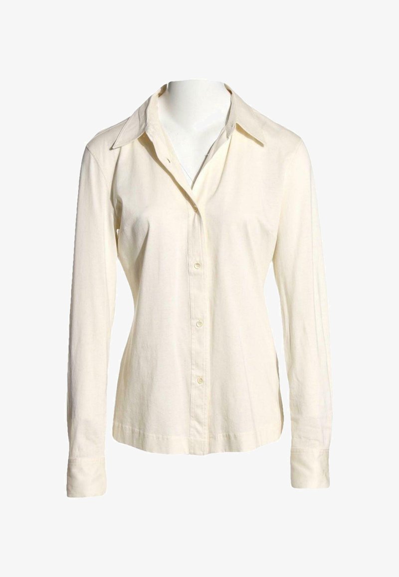 Chemise crème à manches longues avec boutons et col pointu, présentée sur un mannequin sans tête sur fond blanc.