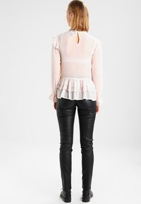 Przezroczysta, jasnoróżowa bluzka z falbaną u dołu, w kropki, z długimi rękawami i dekoltem w kształcie łezki z tyłu; zestawiona z dopasowanymi czarnymi skórzanymi spodniami.