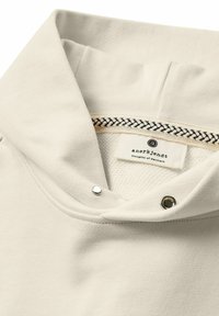 Weißer Pullover mit hohem Kragen, ausgestattet mit einem strukturierten Innenfutter, schwarz-weißem Streifenakzent und Druckknopfdetails.