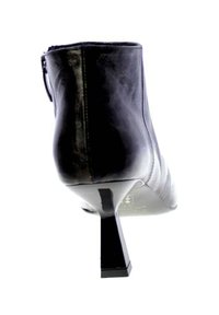 Stivale alla caviglia in pelle nera con punta affilata e tacco sottile di altezza media, visto da dietro su sfondo bianco.