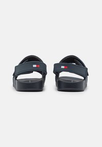 Granatowe sandały z regulowanymi paskami i gumową podeszwą. Posiadają mały detal z logo w kolorze czerwonym i białym na pasku. Teksturowana wkładka.