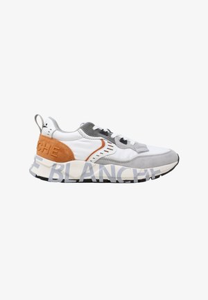 Sneaker bianca e grigia con tallone in suede marrone e grande testo stampato sulla suola, con lacci neri e bianchi.