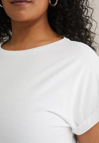 Top blanco de manga corta con escote redondo, hecho de una tela suave. Diseño sin costuras y textura suave, que acentúa el escote.