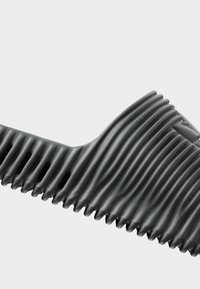 Black flexible corrugated plastic tube with a curved bend section against a light grey background.