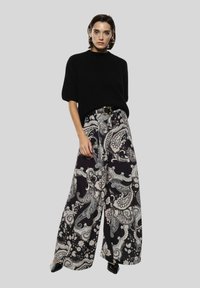 Maglione nero lavorato a maglia con maniche ampie abbinato a pantaloni palazzo a vita alta con motivo nero e crema, caratterizzati da un design paisley.