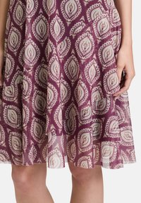 Lila Kleid mit einem Blattmuster in Beige und Creme. Leichter, fließender Stoff mit einem gestuften Saum und leicht durchscheinender Textur.