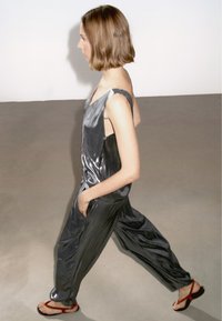 Metallisk grå ärmlös jumpsuit med V-ringning, lös passform, sidofickor och mjuk textur, kombinerad med röda flip-flops.