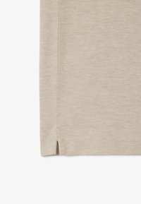 Beige textil med en strukturerad yta och ett subtilt mönster. Nederkanten har sidoinsnitt som ökar flexibiliteten och komforten i designen.