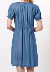 Vestido de mezclilla con mangas cortas abullonadas, puños elásticos, cintura ceñida y corte relajado. Color azul claro, textura suave, longitud a medio muslo.