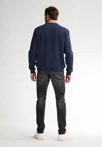 Marineblaues Sweatshirt mit gesprenkelter Textur, Rundhalsausschnitt und gerippten Bündchen, kombiniert mit verblassten grauen Slim-Fit Jeans und weißen Sneakers.
