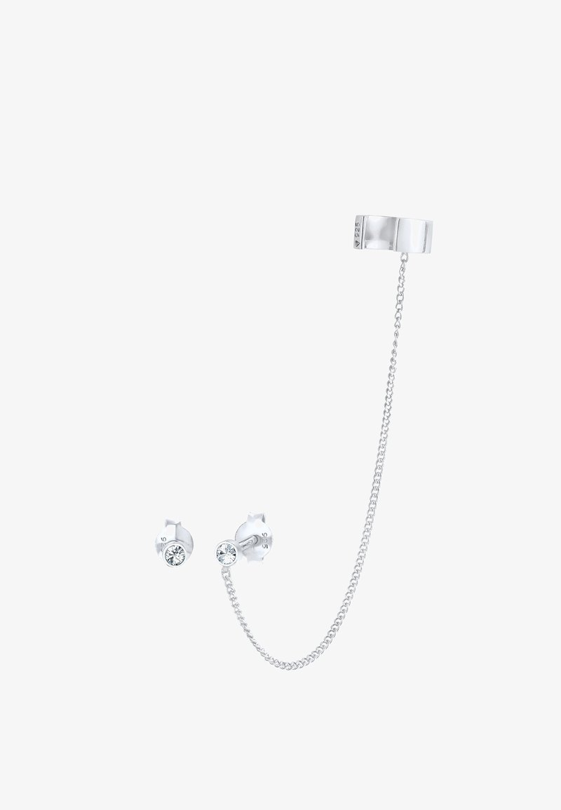 Manchette d'oreille argentée reliée par une chaîne à des clous d'oreilles en argent avec des pierres précieuses rondes claires sur fond blanc.