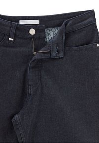 Jeans de mezclilla oscura con cierre de cremallera y botón, con una textura suave y detalles de costura sutiles. El forro interior presenta un patrón de logo.