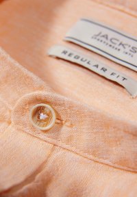 Tessuto di camicia arancione chiaro con una trama tessuta, caratterizzato da un bottone color crema e etichette con la scritta "JACK’S" e "REGULAR FIT."