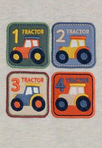 Vier bestickte Patches mit Traktoren in Orange, Gelb, Blau und Creme, jeweils nummeriert von 1 bis 4, auf bunten quadratischen Hintergründen.