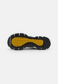 Mustard ja musta sportlik jalatsite  talla osa, mis sisaldab tekstuuriga kollast kummiosa, millel on ruuduline muster, ümbritsetud mustade kummist profiilide ja soontega.