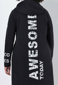 Zwarte hoodie met grote witte tekst "AWESOME" en "TODAY" verticaal op de achterkant. Lange mouwen met kleinere tekst op de cuffs.