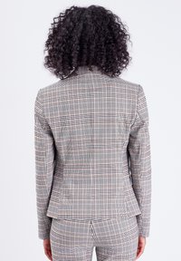 Grijze geruite blazer met een getailleerde vorm, voorzien van een ruitpatroon in zwart en oranje accenten. Gladde stof met gestructureerde schouders.