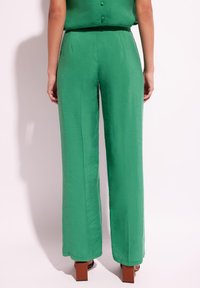 Zielone, wysokie spodnie wykonane z lekkiego materiału. Charakteryzują się prostą nogawką i gładką teksturą, w zestawieniu z obuwiem na bloku.