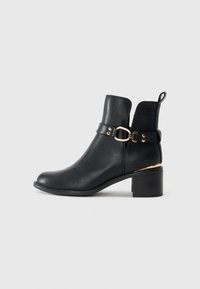 Black leather ankle boot with a rounded toe, gold hardware accent, and a low block heel. Features a flat heel and a loop on the back.