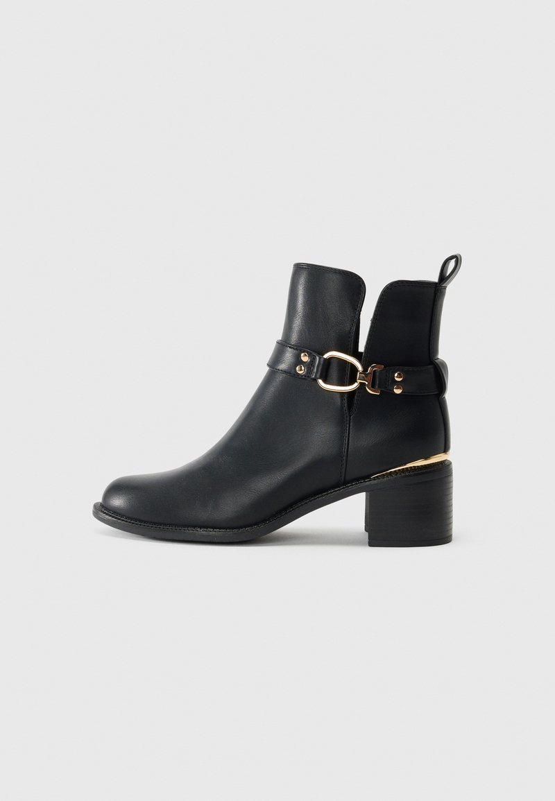 Black leather ankle boot with a rounded toe, gold hardware accent, and a low block heel. Features a flat heel and a loop on the back.
