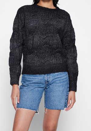Schwarzer gestrickter Pullover mit strukturiertem Muster, runden Ausschnitt und gerippten Bündchen, kombiniert mit zerrissenen Jeansshorts.