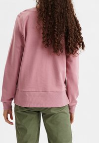 Rosa sweatshirt med avslappnad passform, ribbade ärmslut och nederkant, tillsammans med gröna byxor. Mjuk struktur och minimalistisk design.