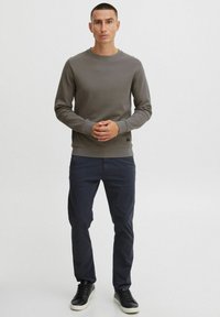 Szary sweatshirt z okrągłym dekoltem i długimi rękawami, z prążkowanymi mankietami i dołem, zestawiony z granatowymi spodniami i czarnymi sneakersami. Minimalistyczny design, bez wzorów.