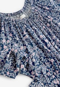 Mörkblå blus med blommönster och rynkad halsringning, prydd med rosa och vita blommor. Lättviktsmaterial med korta ärmar och elastisk fåll.