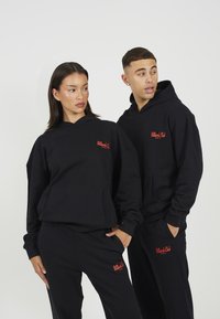 Μαύρες μπλούζες φούτερ με μπροστινές τσέπες, με κόκκινο κείμενο "Billiards Club" στο στήθος. Και οι δύο φορούν ταιριαστά μαύρα παντελόνια, δημιουργώντας μια συντονισμένη εμφάνιση.