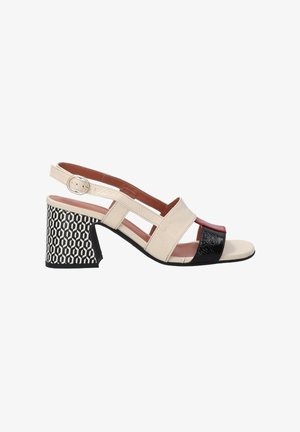 Beige and black slingback sandal with textured and smooth surfaces, block heel featuring a geometric pattern, adjustable ankle strap.