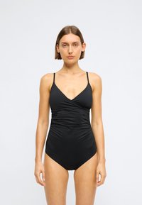 Costum de baie întreg, negru, cu bretele subțiri, detalii din țesătură plisată și un decolteu adânc în V. Material neted, elastic.