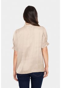 Blusa in satin beige con maniche corte a sbuffo, collo alto e una texture liscia. La parte posteriore presenta una leggera pince per un tocco di stile in più.