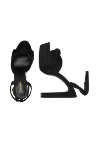 Černé sandály na vysokém podpatku s detailem uzlu, z materiálu semiš, otevřená špička a řemínky kolem kotníku. Podešev je plochá s blokovým podpatkem.