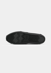 Semelle de chaussure noire avec une surface en caoutchouc texturée, présentant des motifs en zigzag et en losange pour l'adhérence et la stabilité. Conception à bout plat et arrondi.