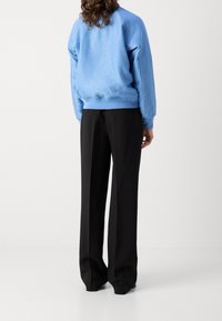 Sudadera azul clara con textura estampada, con puños y dobladillo de canalé, combinada con pantalones acampanados negros, vista desde la parte de atrás.