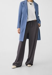 Světle modrý dlouhý kabát, bílé tričko, tmavě šedé široké kalhoty a béžové boty. Má stahovací pásek v pase a vrstvený vzhled.