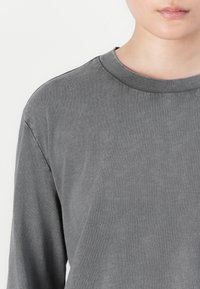 Gray long-sleeve shirt featuring a rounded neckline and textured fabric. Simple design with no visible patterns or hardware details.