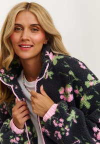 Flísová bunda so sivým základom, kvetinovým vzorom v ružovej a zelenej farbe, so zipsovým uzáverom, ružovými lemami a elastickými manžetami. Mäkko, textúrovaná tkanina.