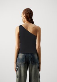Haut noir à une épaule avec une texture côtelée, associé à un pantalon cargo en denim ample avec des poches arrière et une poche rabat sur le côté.