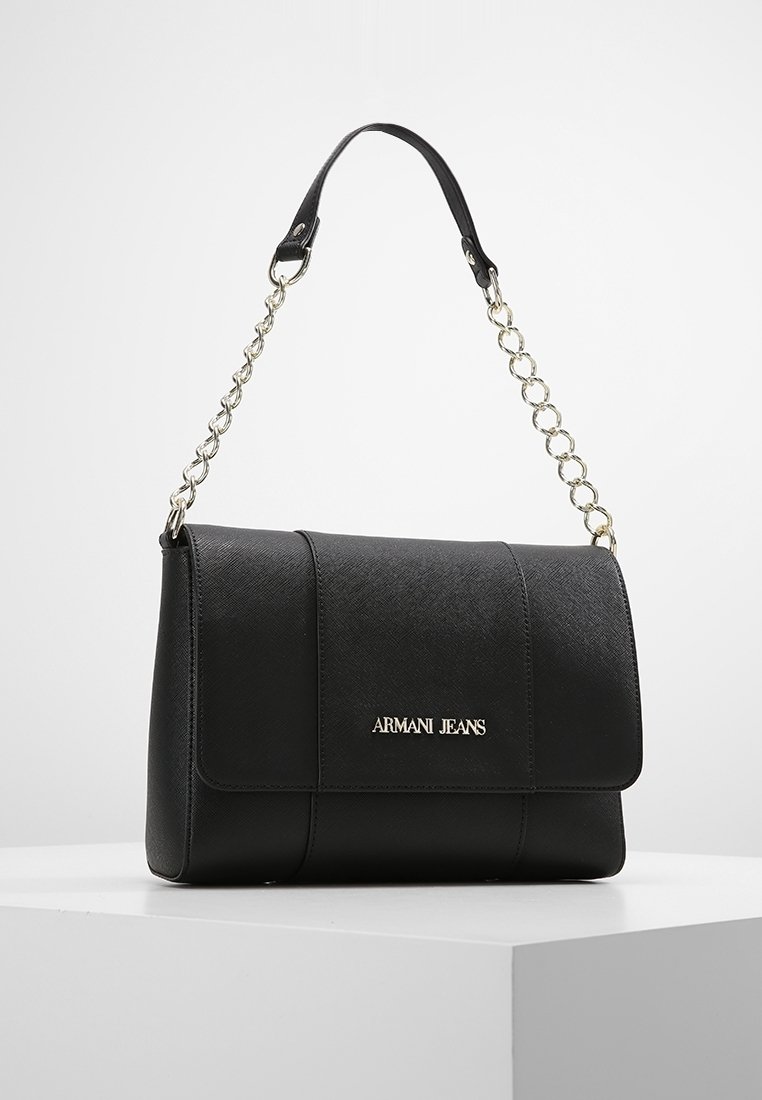 Borsa a spalla nera in jeans Armani con finitura testurizzata e tracolla in catena dorata esposta su un piedistallo bianco.